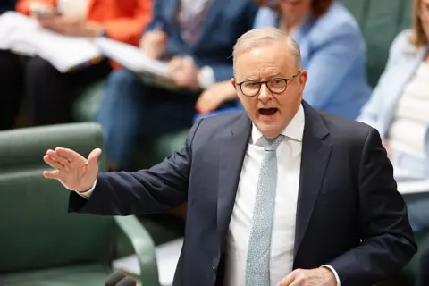 Getty A middle aged man with thinning grey hair and glasses, wearing a suit and tie, gestures as he addresses parliament