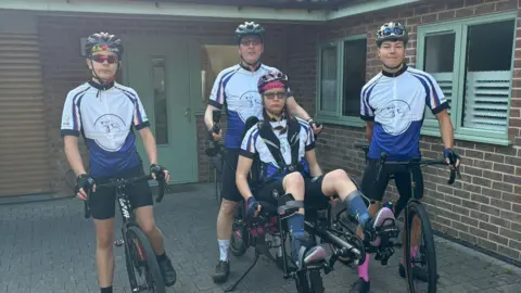 Chloe can be seen sitting on the dual purpose bike.
Her dad Tom is sat behind her,
Her brothers Nicko and William are with their bikes standing next to their sister.
They are outside in front of a building.