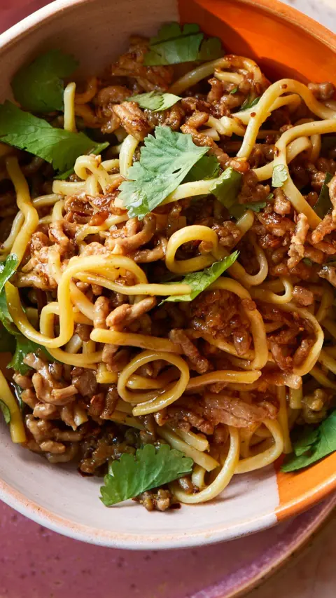 Top down view of noodles and minced pork in an orange and pink bowl