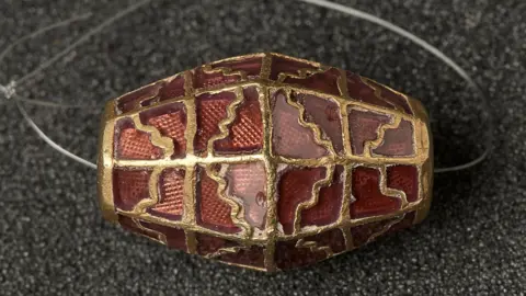 Suffolk County Council A red bead with gold details is pictured resting on a surface. A plastic loop is fitting through the bead.