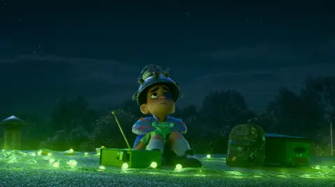 Disney A still image from Elio. Elio sits surrounded by festoon lights. He wears a colander on his head and is staring up at the dark sky,