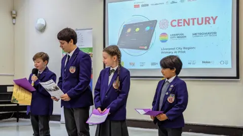 Four school pupils in purple blazers address an open day. A boy on the far left is addressing an audience with a microphone