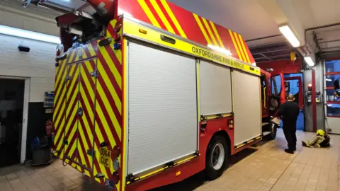 Green Party A fire engine parked up inside a building with a firefighter stood next to it.