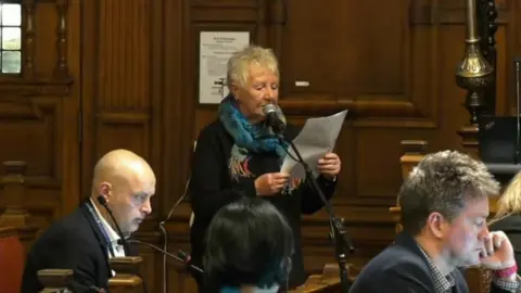 Oxford City Council YouTube A woman is standing in front of a microphone at a council meeting. She is reading from a script