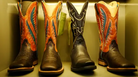 Xiqing Wang/BBC A row of three cowboy boots in orange, back and blue. They are in a box, facing forward. They are patterned on both the leather and the material tops