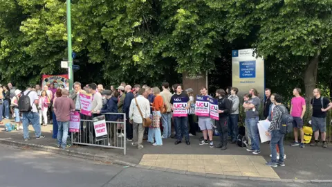 BBC A group of staff and students stood with protest signs outside a university campus.