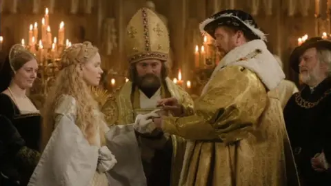 Damian Lewis as King Henry VIII putting a ring on the finger of Kate Phillips as Jane Seymour in a wedding ceremony in a scene of Wolf Hall