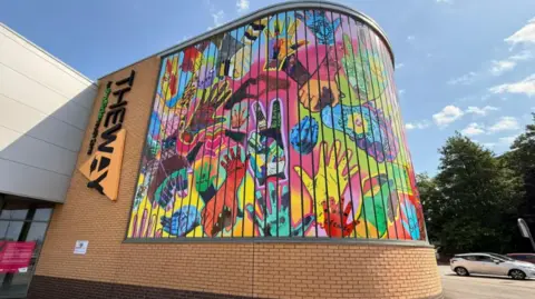 The Way Colourful artwork covers the curved corner of the youth centre amid brickwork. 