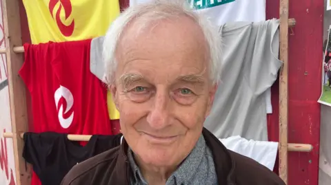 A man with white hair is seen smiling at the camera
