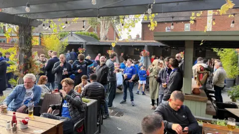 Dan Lightfoot/The Greyhound A view of a pub beer garden filled with football fans. Many fans have drinks in their hands or on tables they sit at. 