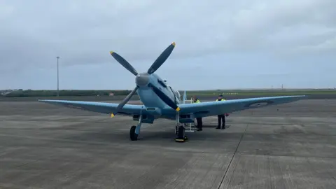The front of the blue spitfire parked on a runway.