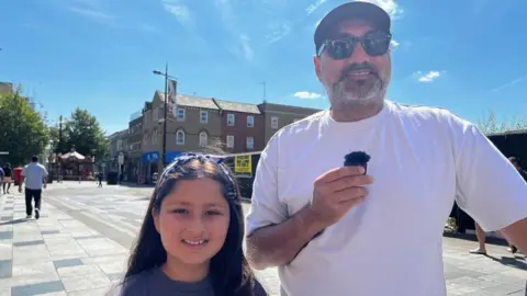 Parmjjt is interviewed in the street with his young daughter.