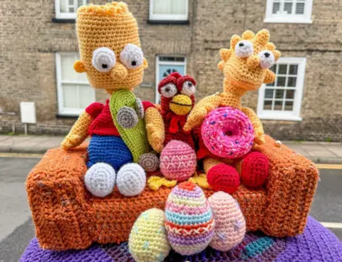 Veronica in the Fens A knitted post box topper features characters from The Simpsons TV cartoon sitting on a sofa surrounded by knitted Easter eggs