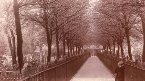 A brown photo of a cemetery with railings on both sides of a path that runs through the middle.