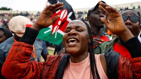 A mourner wearing red jacket and with braids wails during the funeral service