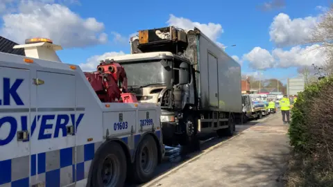 Andy Trigg/BBC A white lorry with a smoke damaged cab attached to a white a blue recovery truck. Two police officers are standing by the lorry