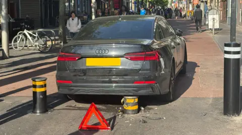A car with a rising bollard touching its underside on High Street, Leicester city centre, on May 2025.