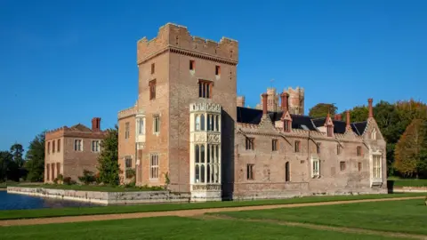National Trust/Mike Selby Exterior of Oxburgh Hall, a brick built 15th Century manor house, surrounded by a moat and under a blue sky