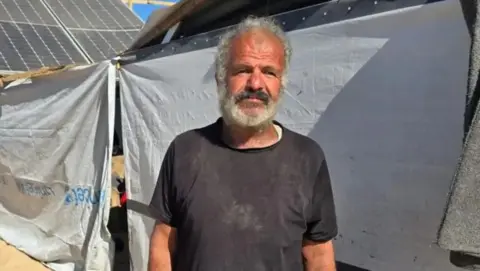 Khaled Halas, an elderly man wearing a black shirt, looks to his left. 