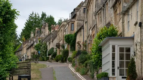View of a street lined with properties and greenery in the town of Burford, UK.