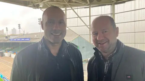 Leon e Geordan sorriram para o estádio Welford Road Stadium ao fundo.