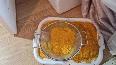 Crown Prosecution Service yellow powder-like substance in a sieve on top of more of the same substance in a white plastic tub on the floor