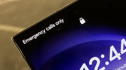 The upper-half of the screen of a mobile phone. It tells us it can make 'Emergency calls only' and there is no reception.
