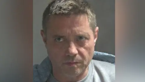A custody photo of John Alford wearing a grey T-shirt or jumper.