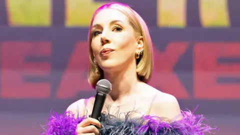 Katherine Ryan holding a microphone while performing in Brighton last month, wearing a frilly purple outfit