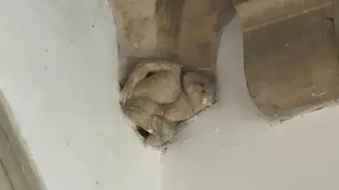 Stone carving of the imp at Grimsby minster. It is portrayed holding its bottom and at the bottom of one of the pillars supporting the tower.