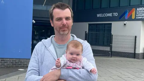 David Lewis holding his baby outside the Blair Mayne leisure centre