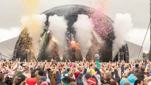 Yellow and pink confetti goes off into the air as a crowd of concert goers jump with their hands in the air during a performance at Kubix festival. 