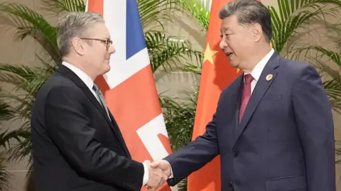 Reuters British Prime Minister Keir Starmer shakes hands with Chinese President Xi Jinping in front of a British and Chinese Flag ahead of their bilateral meeting 