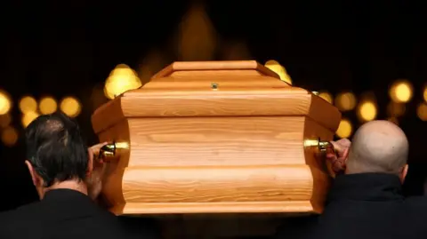 An image from behind a coffin being carried on the shoulders of two men