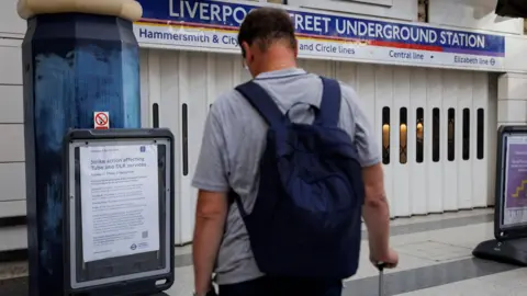 EPA A man stands with his back to the camera looking at an information board. In front of him is the shuttered entrance to a Tube stations. 