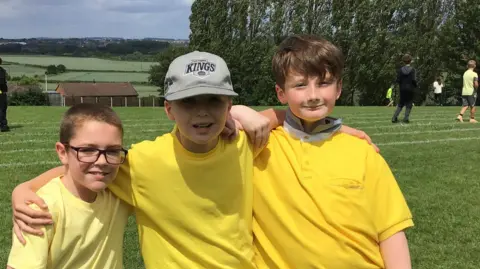 WINDHILL PRIMARY SCHOOL, MEXBOROUGH Three boys on a playing field in yellow tops put arms round each other and pose for the camera