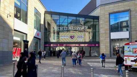 BBC The Broadway shopping centre in Bradford, with an ice cream van outside and several people walking in and out.