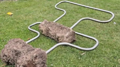 The two railings and their connected concrete footings lie on the grass following the vandalism. 
