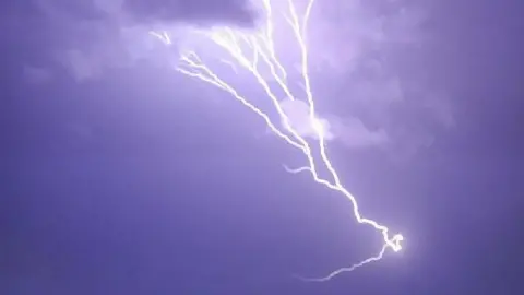 A large fork of lightning streaks across a purple sky. 