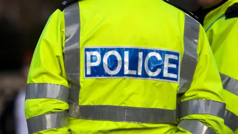 Close up of officer's with the words 'police' on. They are wearing a yellow high vis jacket. 