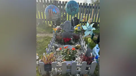 Handout A baby's grave. It is covered in flowers and toys. 