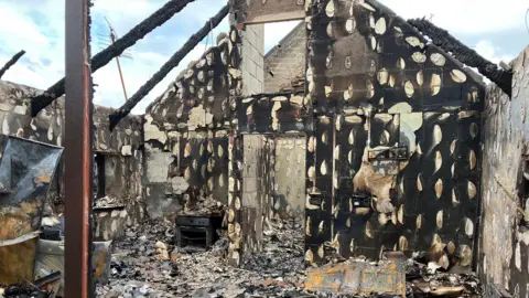 One of the burnt out houses is full of ash and black burn marks cover the walls.
