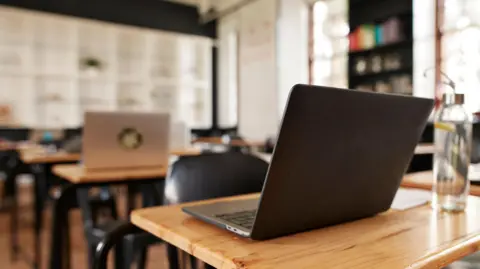 A number of laptops on a row of school desks