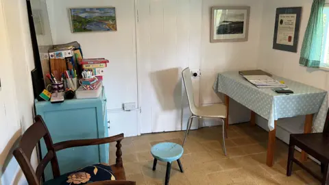 An interior view of the bungalow, showing a table and chair as well as a blue chest of drawers