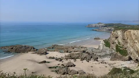 A view of a Cornwall beach. It shows rugged cliffs and sandy beaches. 