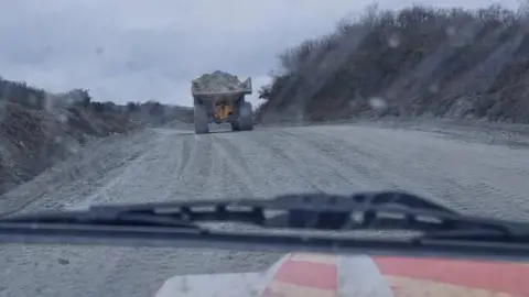 A large truck driving through a clay pit carrying heavy material
