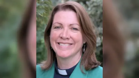 Diocese of Winchester Rhiannon King from the shoulders up. She is wearing a green blazer, black shirt and dog collar.