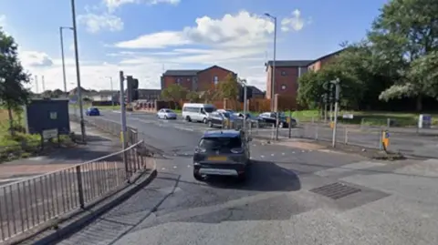 Google The East Lancashire Road at its junction with Stonebridge Lane in Croxteth, there are cars on the road on either side of the junction.