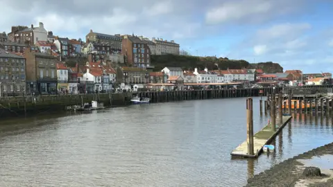 Carla Fowler/BBC Whitby harbour with houses and shops on one side and several fishing boats moored up 