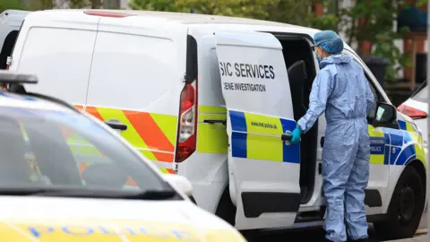 A forensics officer opens the door of a police van while wearing a hazmat suit at the scene in Finchley on Wednesday.